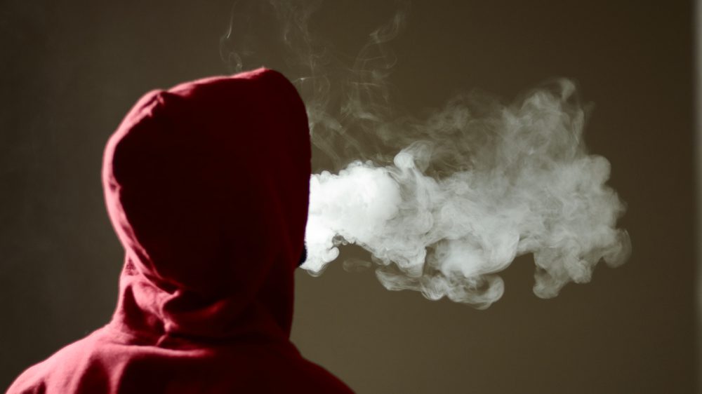 Young,Male,In,Red,Hoodie,Vaping,Smoking,,Exhales,Thick,Vapor,